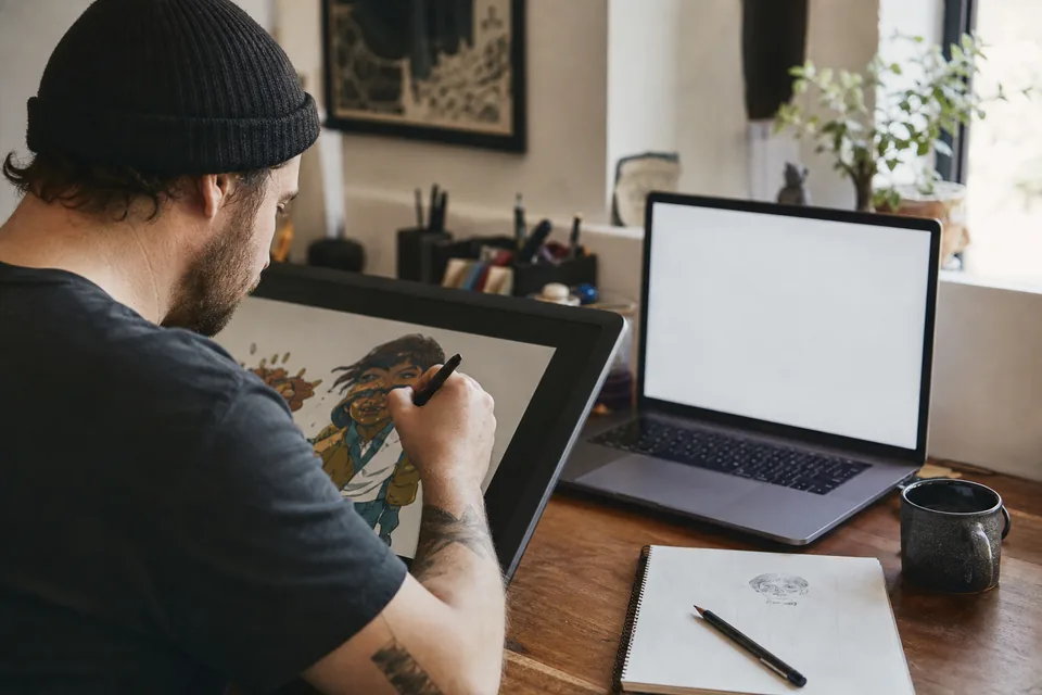 Illustrator at a home studio desk with a drawing tablet and a laptop open to a billing screen